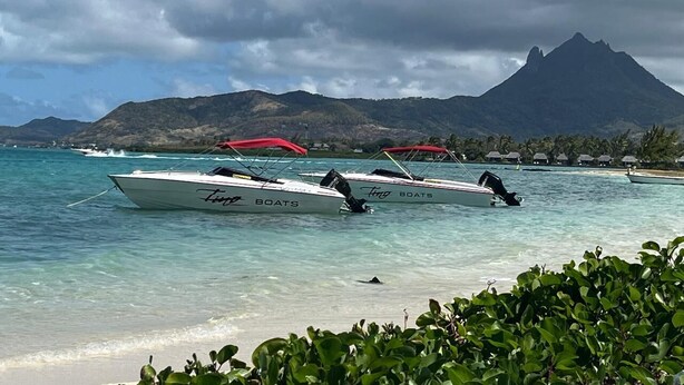 Une plage où sont amarrés des bateaux, une eau turquoise et limpide, et une montagne en arrière-plan.