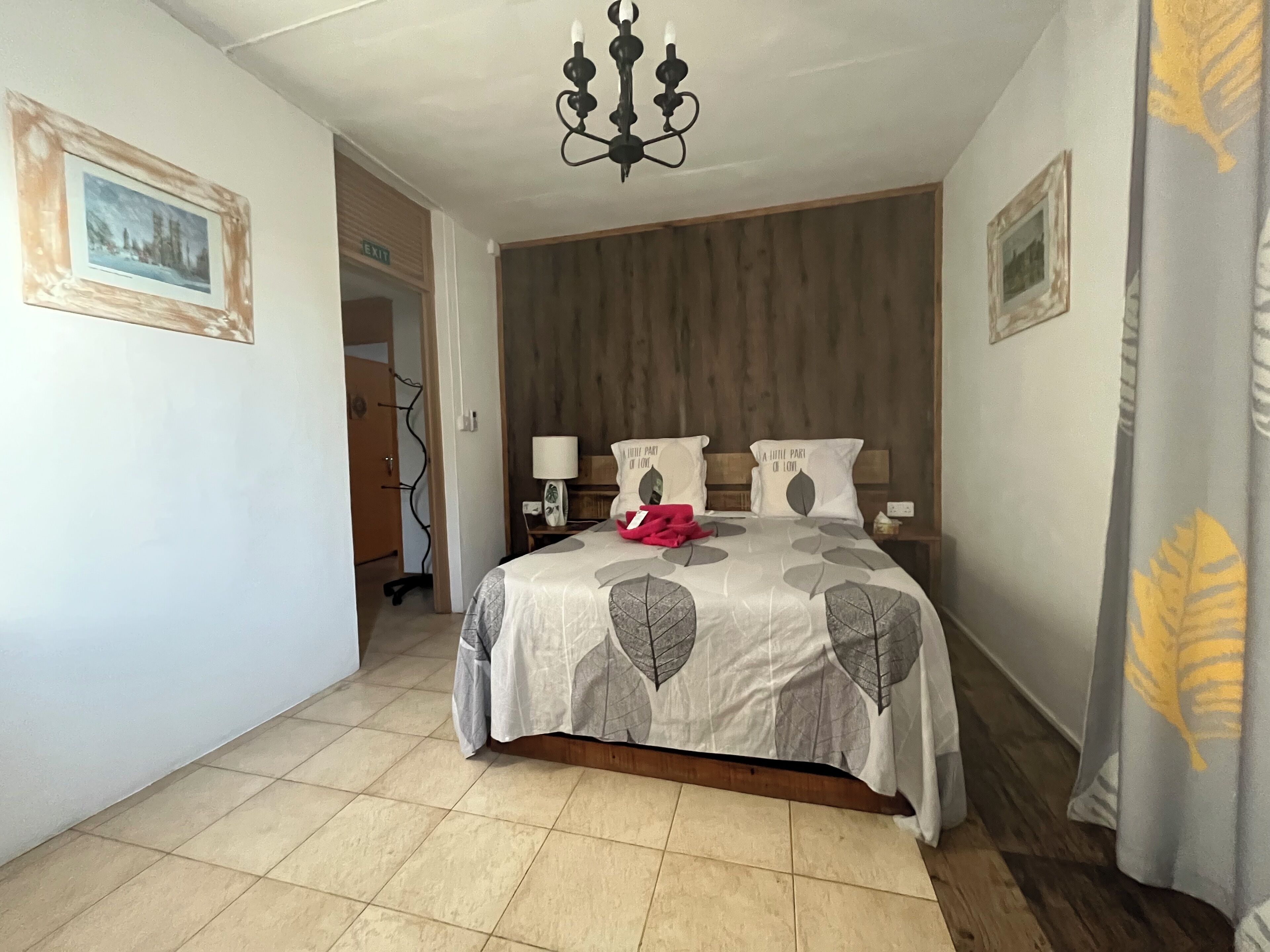 A bedroom with a bed, a chandelier, a wooden headboard, a nightstand, and a door leading to another room.