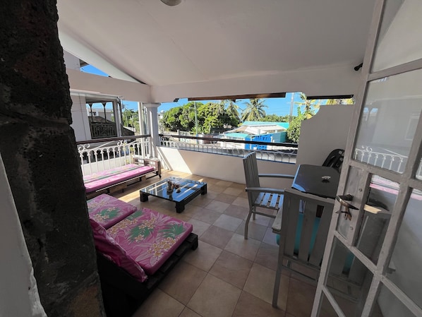 A balcony with two beds, a table, and a chair.