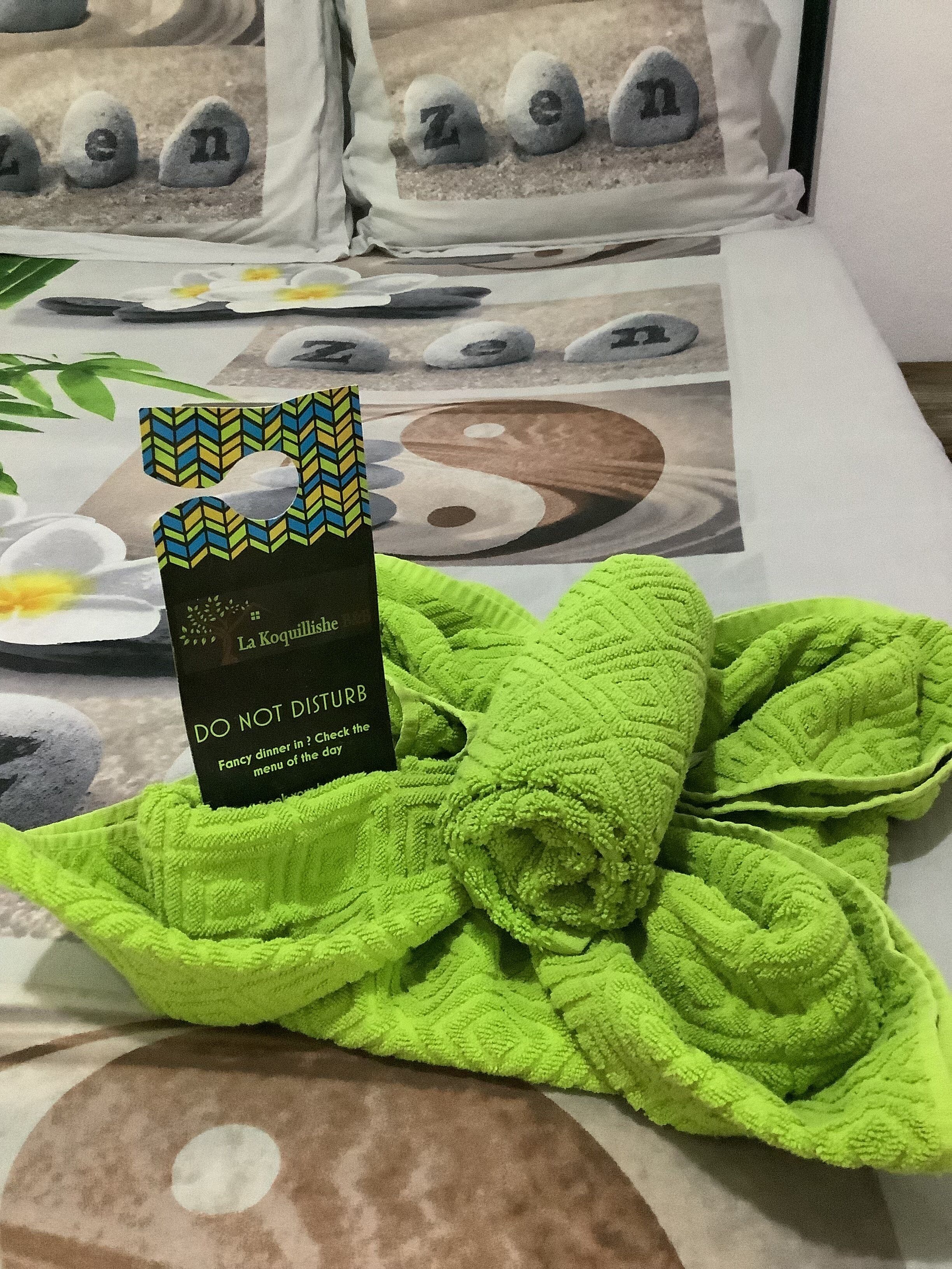 A green towel on a bed with a Zen-themed bedspread.