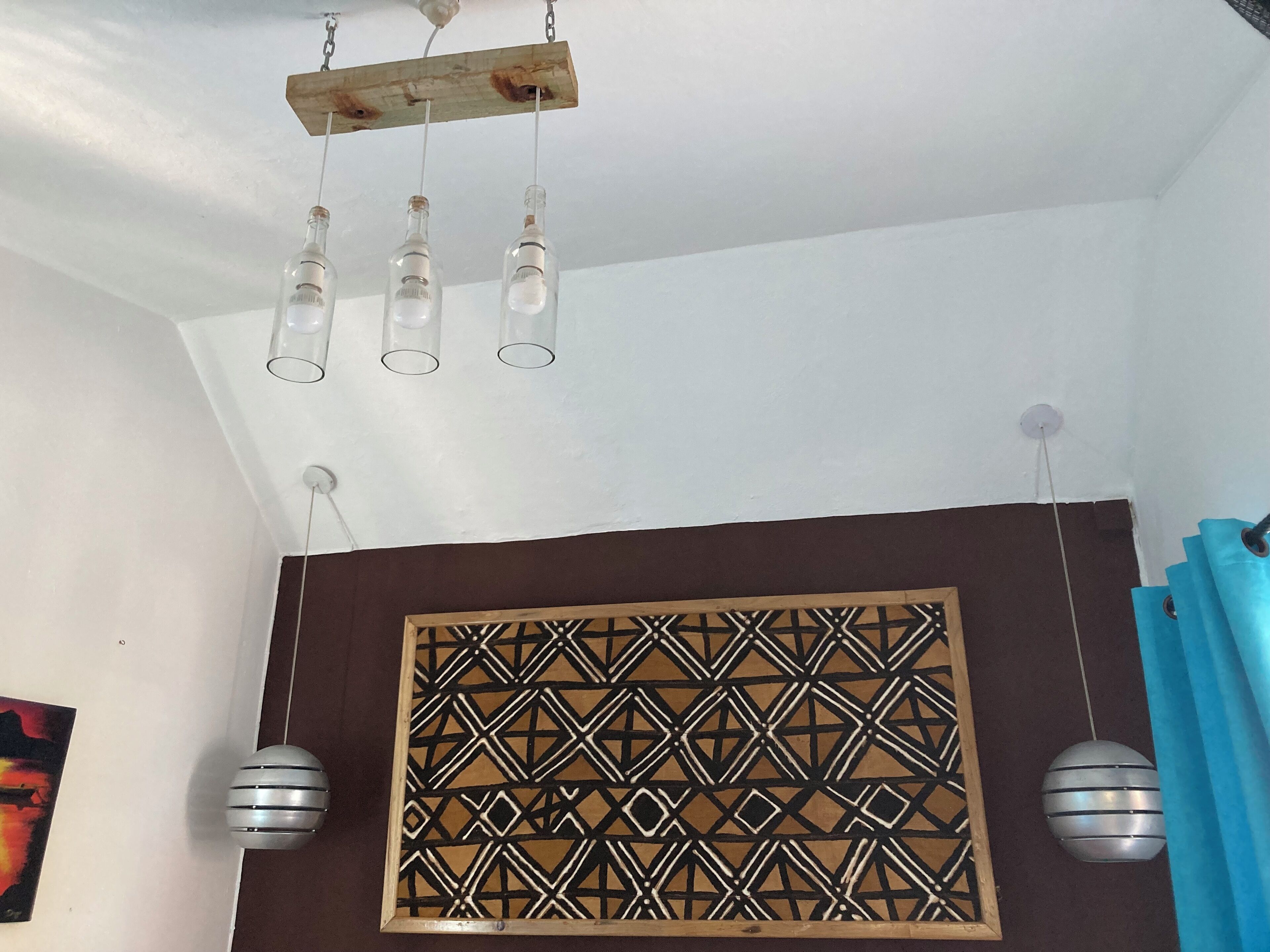 A room with a geometric patterned wall panel, a wooden ceiling with hanging light fixtures, and a blue curtain.