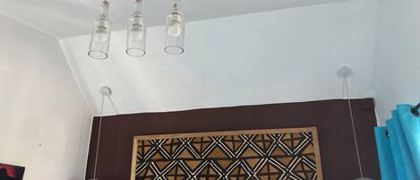 A room with a geometric patterned wall panel, a wooden ceiling with hanging light fixtures, and a blue curtain.