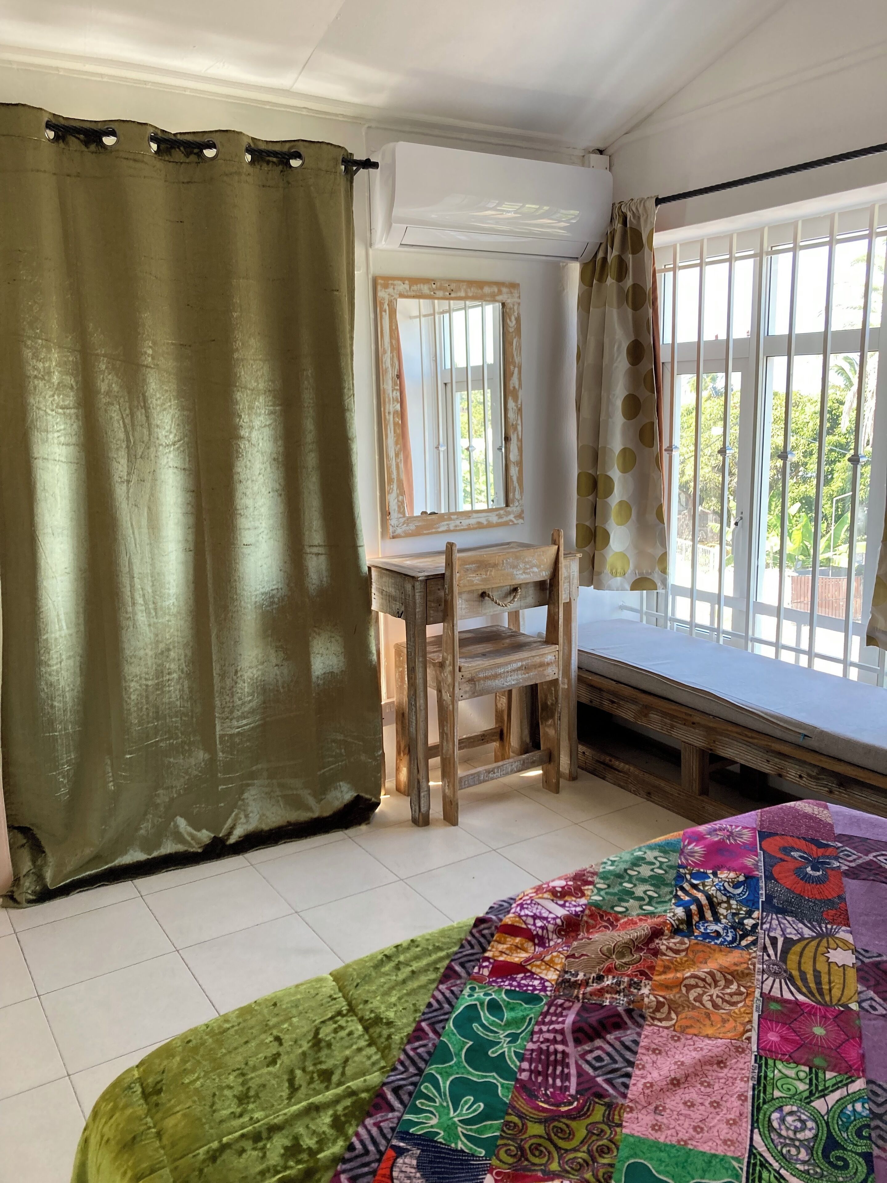 A room with a bed, a wooden chair, a window with bars, and a curtain.