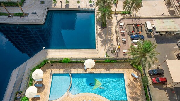 An aerial view of a hotel with two swimming pools, one larger and one smaller, surrounded by palm trees and lounge chairs. - Large 1BR with Lake View in JLT  Close to Metro (Dubai)