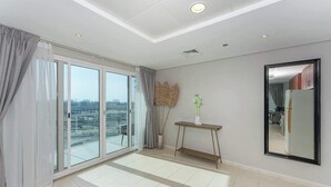 A modern hotel room with large floor-to-ceiling windows, a view of the cityscape, a small console table with a vase, and a large mirror on the wall. - Large 1BR with Lake View in JLT  Close to Metro (Dubai)