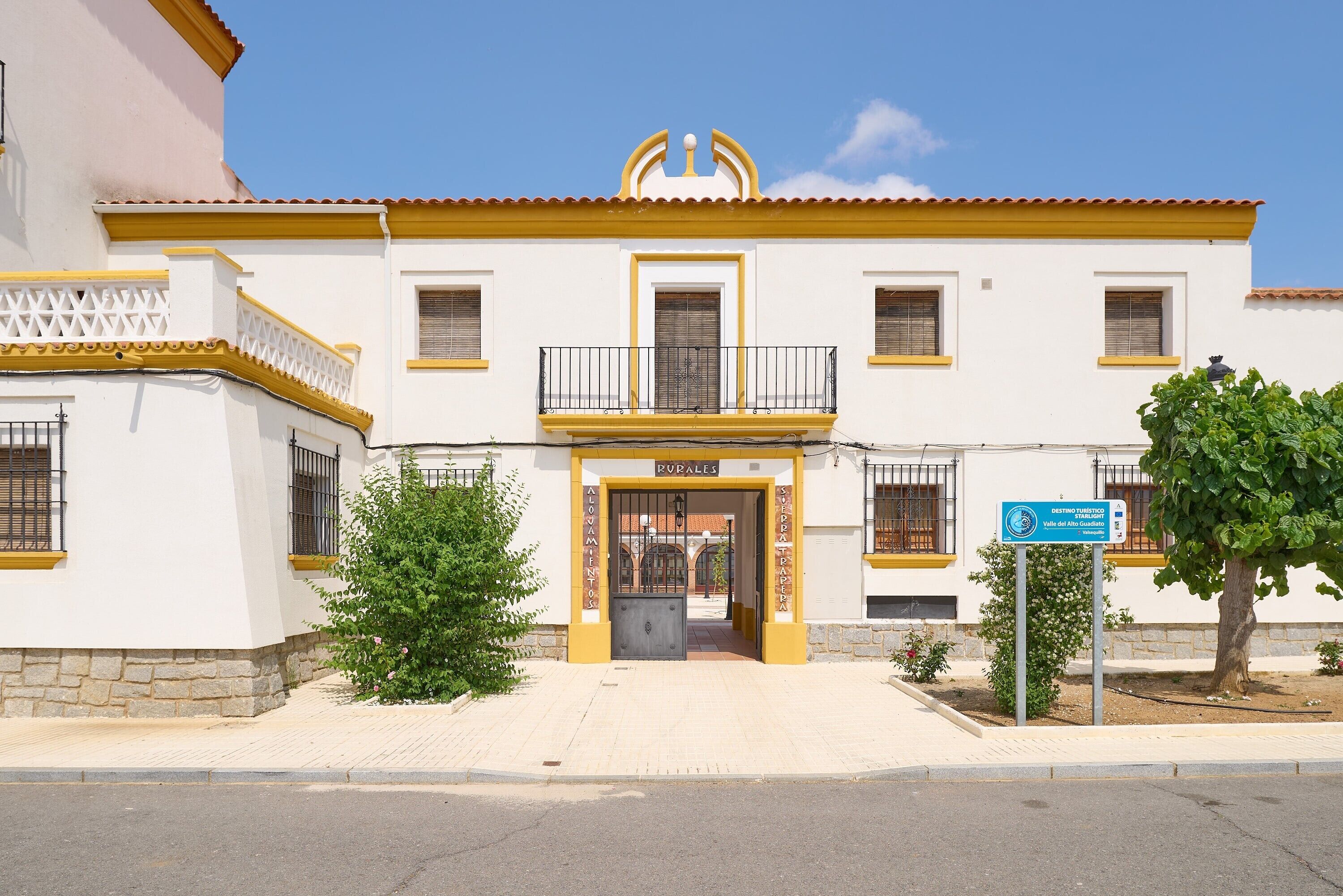 Un edificio con fachada amarilla y blanca, una entrada central con portón y un letrero que indica un destino.