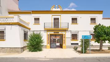 Un edificio con fachada amarilla y blanca, una entrada central con portón y un letrero que indica un destino.
