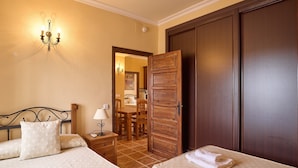 A hotel room with two beds, a wooden wardrobe, a chandelier, a dining area, and a bathroom. - Apartment 'Jazmin' with Balcony, Wi-Fi and Air Conditioning (Valsequillo)