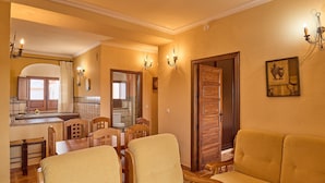 A dining area with wooden chairs and a table, a sofa, a kitchen with a window, and a door leading to another room. - Apartment 'Jazmin' with Balcony, Wi-Fi and Air Conditioning (Valsequillo)