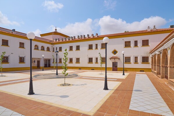A courtyard with tiled flooring, lamp posts, and a building with multiple windows and a tiled roof.