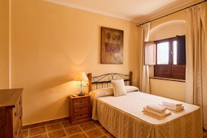 Une chambre à coucher avec un lit, une table de chevet avec une lampe, une commode, une fenêtre avec des rideaux et un tableau au mur.
