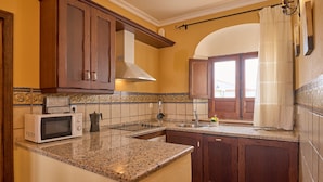 A kitchen with wooden cabinets, a microwave, a sink, and a window with a curtain. - Apartment 'Jazmin' with Balcony, Wi-Fi and Air Conditioning (Valsequillo)