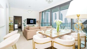 Un salon moderne avec un canapé beige, des fauteuils blancs, une table basse en verre et un téléviseur fixé au mur.