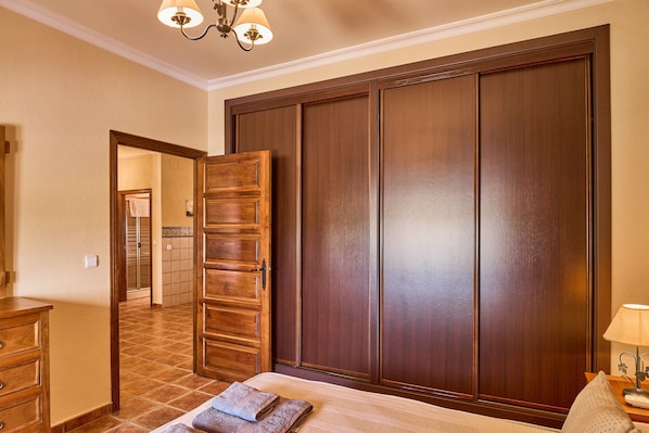 A bedroom with a large wardrobe, a bed with a striped bedspread, and a nightstand with a lamp.
