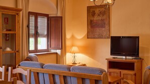 Una sala de estar con un sofá, sillas de madera, un televisor, una lámpara y una ventana con persianas.
