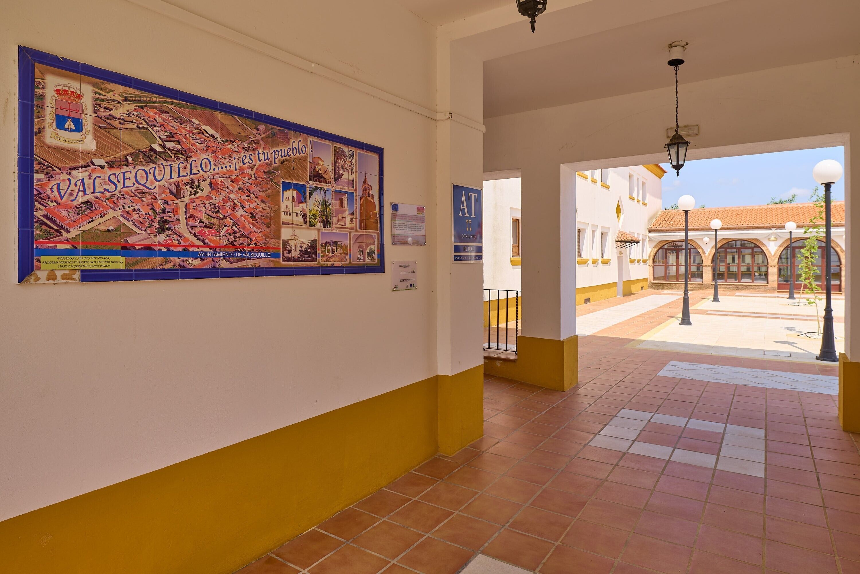 A corridor with a tiled floor, a poster on the wall, and an open doorway leading to an outdoor area with a tiled roof.