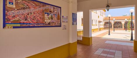 A corridor with a tiled floor, a poster on the wall, and an open doorway leading to an outdoor area with a tiled roof.