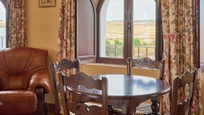 Un coin repas avec une table ronde et des chaises, un fauteuil en cuir, une fenêtre donnant sur des champs et un tableau encadré au mur.