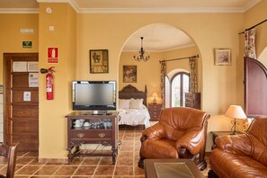 Habitació d'hotel amb televisió, butaques de pell, un llit, una llar de foc i un passadís que condueix a una altra habitació.