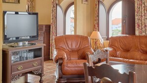 Un salon avec un téléviseur, des fauteuils en cuir, un meuble en bois et des rideaux à motifs floraux.