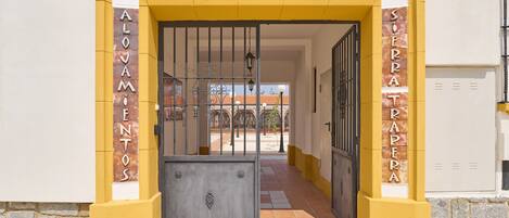 A building entrance with a yellow and white facade, a metal gate, and the words 'Rurales' and 'Alovamientos' on the pillars.