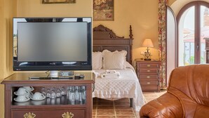 Une chambre d’hôtel équipée d’une télévision, d’un lit avec du linge de maison blanc, d’une commode en bois avec de la verrerie et d’un fauteuil en cuir.