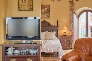A hotel room with a television, a bed with white linens, a wooden dresser with glassware, and a leather armchair. - Apartment 'Alheli' with Balcony, Wi-Fi and Air Conditioning (Valsequillo)