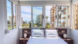 A bedroom with a bed, two bedside tables, a window with a view of a residential area and a body of water. - Apartment 'Sol and Sea A121' with Sea View, Wi-Fi and Air Conditioning (El Morche)