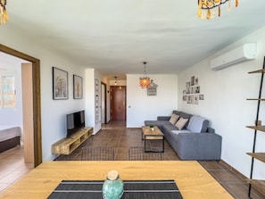 Un salon moderne avec un canapé, une table basse et un téléviseur. On y trouve également un banc en bois et une plante décorative.
