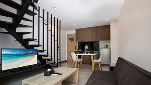 Un espace de vie moderne comprenant un téléviseur diffusant une scène de plage, un coin repas avec une table et des chaises, un canapé et un coin cuisine équipé d’une cuisinière et d’un réfrigérateur.