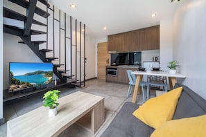 Una sala de estar moderna con una televisión, una mesa de centro de madera, un sofá con cojines amarillos, una escalera y una zona de cocina.