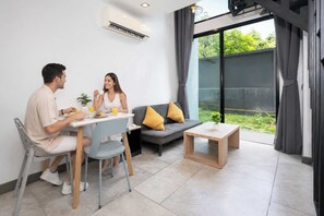 A modern living room with a dining area, a sofa, a coffee table, and a large window with curtains.