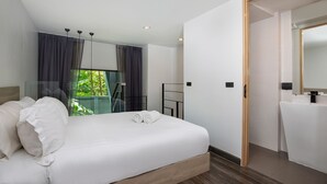 Une chambre d’hôtel moderne avec un grand lit, une salle de bain avec un miroir et une vue sur la verdure environnante.