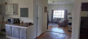 A living room with a sofa, a coffee table, and a window with curtains. There is a door leading to another room. - Villiers Villa (Gqeberha)