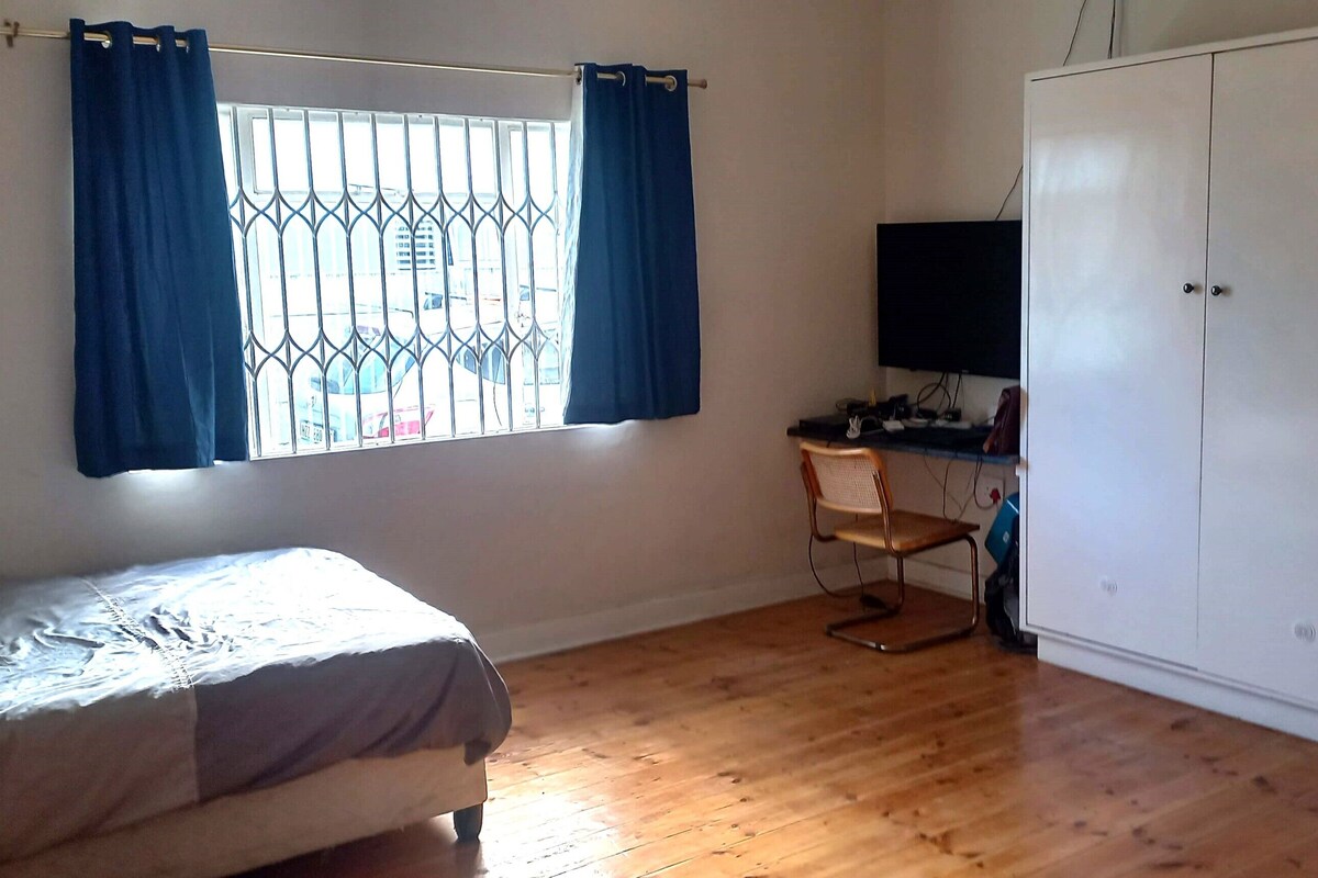 A bedroom with a bed, a desk with a chair, a wardrobe, and a window with curtains.