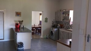 A compact kitchen with a washing machine, a dining area with chairs, and a refrigerator. - Villiers Villa (Gqeberha)