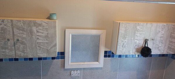A bathroom with two wooden cabinets, a framed mirror, and a blue-tiled backsplash.