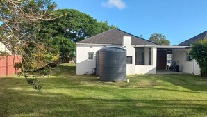 A two-story house with a large water tank in the yard, a covered porch, and a small attached garage. - Villiers Villa (Gqeberha)