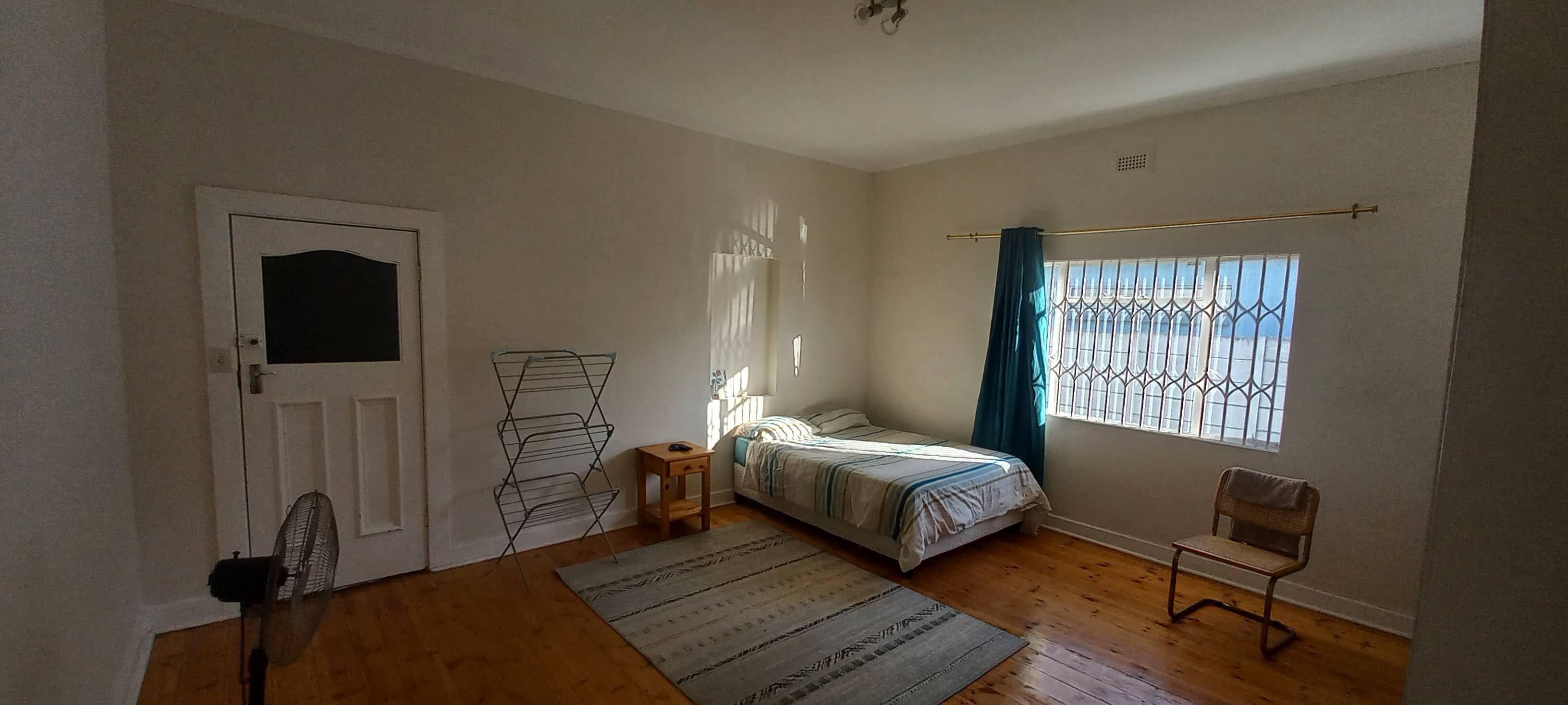 Une chambre à coucher avec un lit, une chaise, un ventilateur, une fenêtre avec des rideaux et une porte.