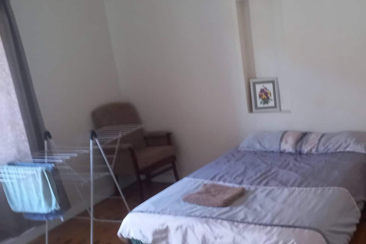 Un dormitorio con cama, una silla, cómoda y estante en la pared.