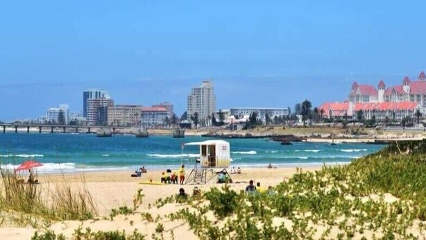 A beach with a lifeguard tower, a pier, and buildings in the background. - Villiers Villa (Gqeberha)