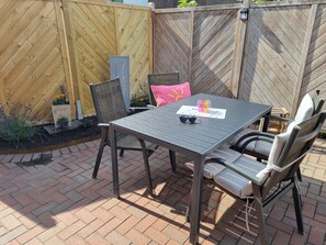 An outdoor patio with a table and chairs, a wooden fence, and a planter with flowers. - 3-room ground-floor apartment near the beach (Büsum)
