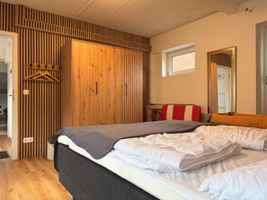 A bedroom with a bed, a wooden wardrobe, a window, and a mirror. - 3-room ground-floor apartment near the beach (Büsum)