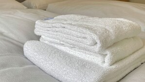 A neatly made bed with white linens, a wooden wardrobe, and a small shelf with a teddy bear. - 2-room apartment on the ground floor close to the beach (Büsum)