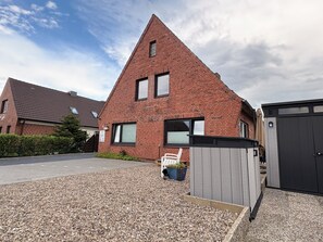 Een huis van rode bakstenen met een schuin dak, een oprit van grind en een houten omheining.