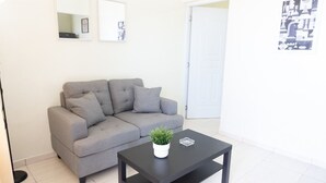 Een moderne woonkamer met een grijze bank, een zwart bijzettafeltje en een kleine plant in pot.