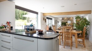 Eine moderne Küche mit einer großen Kochinsel, einem Holzespeisetisch und Stühlen. Es gibt Schränke, eine Spüle und verschiedene Küchenutensilien auf der Arbeitsplatte.