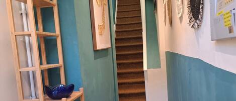 A hallway with a wooden ladder, a blue wall, a staircase, and patterned floor tiles.