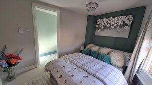 Un dormitorio con cama, lámpara de pared, ventana con cortinas y puerta que da a otra habitación.