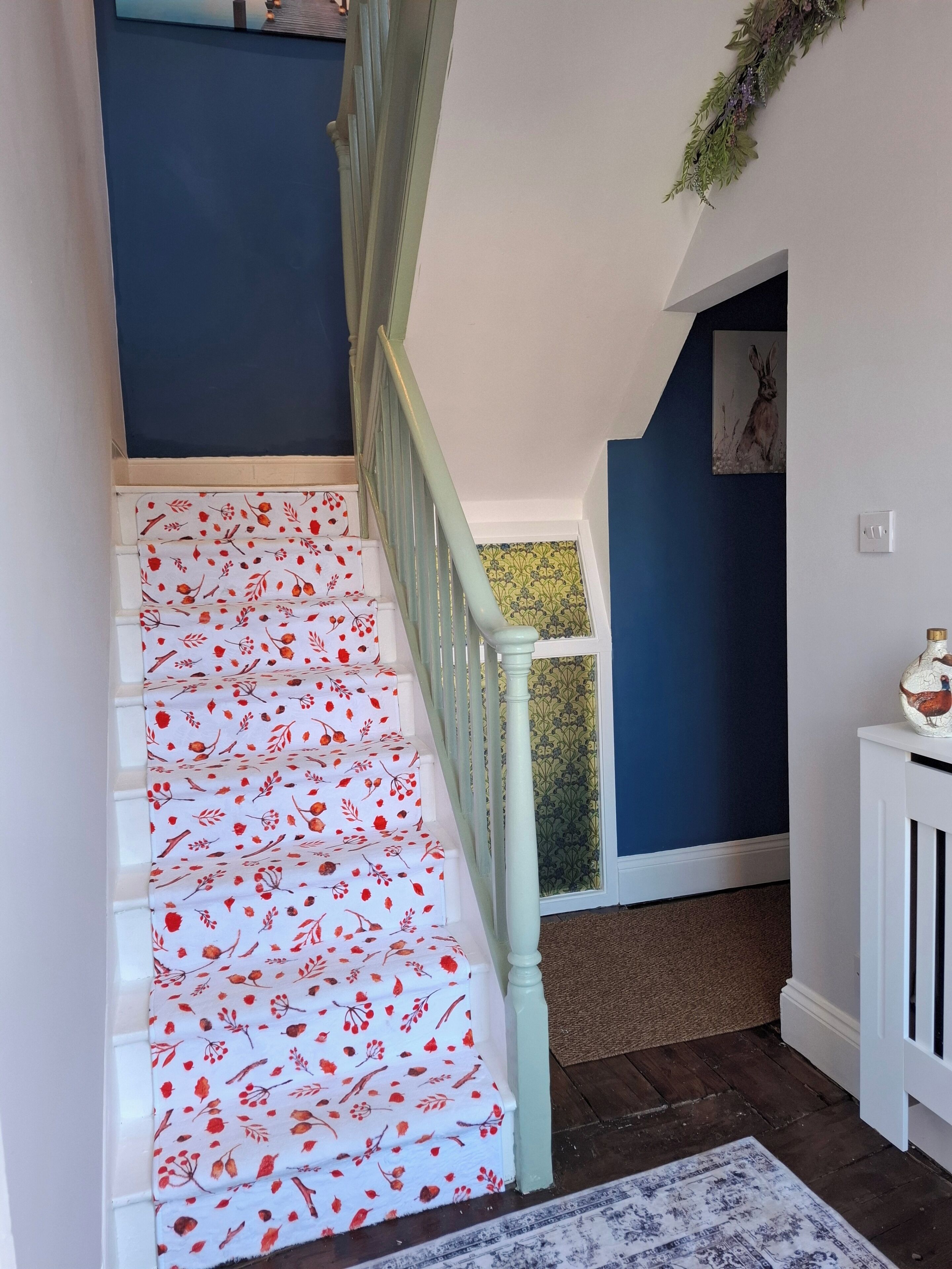 A staircase with white steps and red floral patterns, leading to a room with blue walls and a framed picture on the wall.
